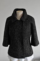 Front view of black textured mid-length jacket on mannequin, showing collar and 3/4 sleeves