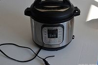 Front view of the Instant Pot showing the digital control panel, black lid, and power cord.