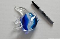 Blown glass fish figurine with blue and white swirls, positioned next to a Sharpie marker for scale