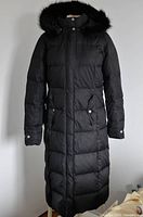Front view of full length black winter coat with fur trimmed hood, button and zipper closure, front pockets with flaps.
