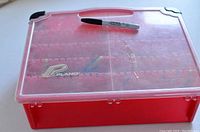 Top view of closed red Plano tackle box with clear lid and black corner protectors, with Sharpie pen for scale.