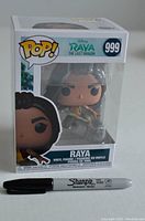 Front view of boxed figure showing Raya character in Funko POP style with Sharpie marker for scale.