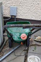 Front view of green plastic hopper and metal frame spreader on concrete with adjustable dial visible