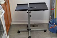 Full view of the metal stand with two black rectangular platforms and caster wheels on the floor.