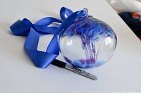 Glass ball with internal blue and purple glass details resting on a flat surface next to a sharpie marker for size reference.