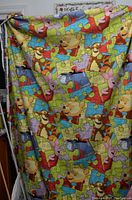 Photo showing the colorful large piece of polar fleece fabric with Winnie the Pooh and friends in a puzzle pattern, held up to display the full print.