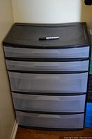 Front view of the large plastic storage unit with five drawers and a black concave top with a marker placed on it for scale.