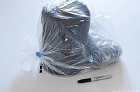 Large roll of black zipper wrapped in plastic with a black zipper pull tab attached, marker for scale.