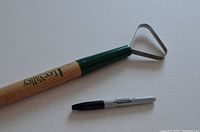 Overall view of the Lee Valley weeding hoe showing wooden handle and triangular metal blade along with black marker for size reference