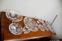Wide angle photo showing all 9 snowflake patterned Mikasa glassware pieces arranged on a wooden surface.