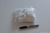 Plastic embroidery floss empty spools in a clear plastic bag with a Sharpie marker for size reference.