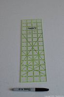 Clear plastic rectangular quilting ruler with green grid lines and angle markings, next to a black Sharpie marker for size comparison.