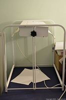 Front view of the white metal frame with height adjustment knob and power cord.