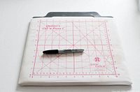 White fabric cover with red grid markings and June Tailor logo, including a Sharpie pen for scale.