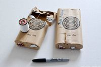 Two packages of white sewing thread with one spool of thread and torn packaging alongside one unopened package and a Sharpie marker for scale.