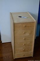 Front view of the tall, narrow wooden storage unit featuring five drawers with small rounded wooden knobs and a light wood finish.
