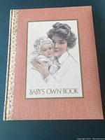 Front cover of Baby's Own Book showing mother and baby illustration with the title on salmon calico padded hard cover