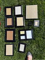 Photo of 11 black picture frames laid out on grass, different sizes and styles, all empty