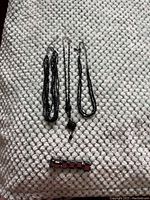 Four pieces of costume jewelry displayed on a textured blanket. Three necklaces made of black chains and beads, plus one bracelet with red and silver square segments.