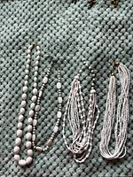 Four white costume jewelry necklaces laid out on a textured surface.