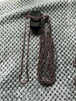 Photo of a dark brown beaded long necklace with tassel and matching beaded bracelet on a textured grey fabric background.