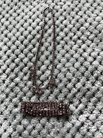 Photo of a silver-tone metal necklace with purple beads and a matching bracelet with purple rectangular stones on a textured grey surface.