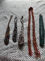Photo showing five costume jewelry necklaces laid out on a textured fabric surface with different colors and textures.