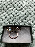 Photo showing three rings on a white foam insert, placed on a textured light grey surface.