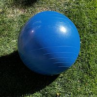 Blue exercise ball resting on grass, showing circular grip lines on the surface and some minor wear marks.