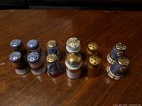 Photo of six sets of vintage salt and pepper shakers placed on wooden surface showing various colors and top holes for seasoning dispensing.