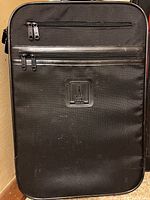 Front view of a black suitcase with front zippered pockets and an Eiffel Tower patch