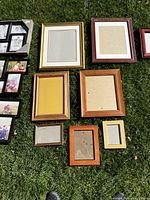 Nine wood picture frames of different sizes and finishes displayed on grass, empty except for the black multi-photo frames with images.