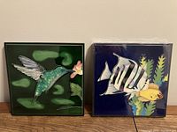Photo of two square art tiles side by side showing a hummingbird on the left and fish on the right.