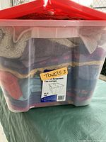 Photo of front side of plastic bin labeled 'Towels 3' showing assorted folded towels inside.