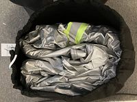 Folded silver car cover inside black carrying bag, showing reflective material and yellow strip