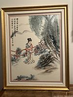 Framed Chinese watercolour painting depicting a woman in traditional dress with calligraphy and red stamps, in a gold frame.