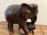 Photo showing full side view of an adult elephant wood carving embracing a calf with its trunk and front leg.