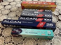 Top view showing all foil, parchment paper, and plastic wrap rolls placed on a lace tablecloth.