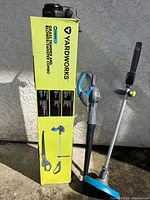 Grass trimmer and blower combo standing next to original yellow box showing product images and brand name.