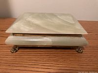 Closed view of a rectangular jade jewelry box with brass trim and claw feet, showing natural patterns in the stone.