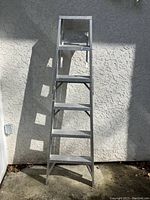Full view of the 6-foot aluminum step ladder standing against a textured white wall in sunlight.