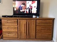 Solid oak Palliser console chest with 9 drawers and two center cabinet doors supporting a TV on top.