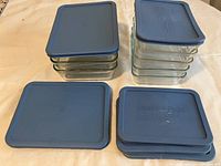 Stack of 3 medium and 5 small rectangular glass containers with blue lids on a light surface.