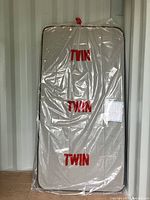 Twin Sealy mattress wrapped in protective plastic cover labeled 'TWIN'.