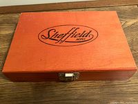 Reddish-brown rectangular wooden box with Sheffield logo on lid and metal clasp.