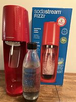 Sodastream Fizzi sparkling water maker in red with carbonating bottle and original box in background
