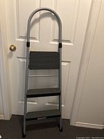 Front view of Cosco 3-step folding stepladder with gray frame and ribbed black steps
