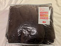 Dark brown Uniqlo HeatTech blanket folded inside original plastic packaging with label stating HeatTech Japan technology, size 200 x 140 cm.
