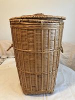 Front view of the tall wicker basket showing vertical weaving pattern and woven loop handles on the sides.