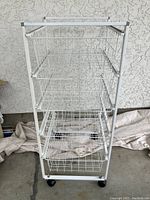 Front view of the 5-tier white wire basket cart standing on caster wheels, showing all five wire baskets and the white metal frame.